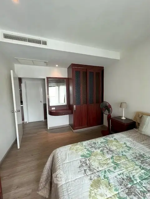 Spacious bedroom with wooden wardrobe and floral bedding in modern apartment.