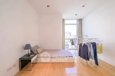 Bright minimalist bedroom with wooden flooring and city view, featuring a cozy bed and clothes rack.