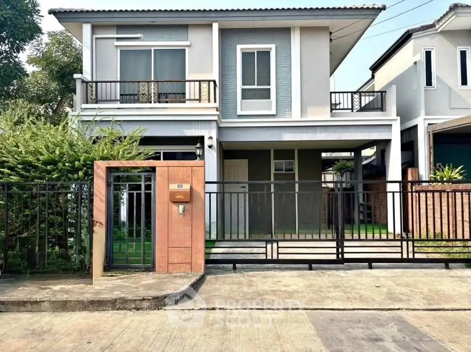 Modern two-story house with gated entrance and balcony in suburban neighborhood.