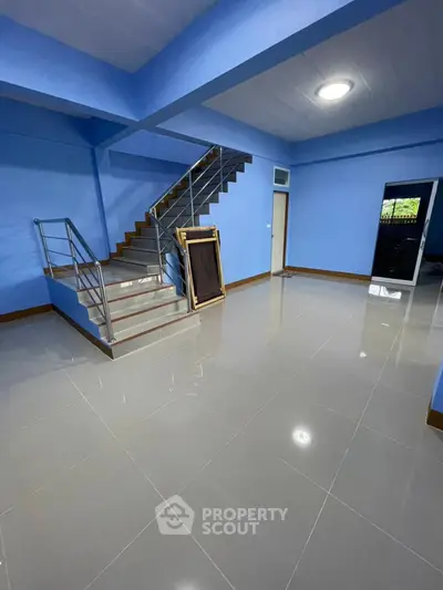 Spacious interior with modern staircase and glossy tiled flooring in vibrant blue setting.