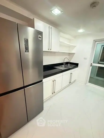 Modern kitchen with sleek stainless steel fridge and minimalist white cabinetry.