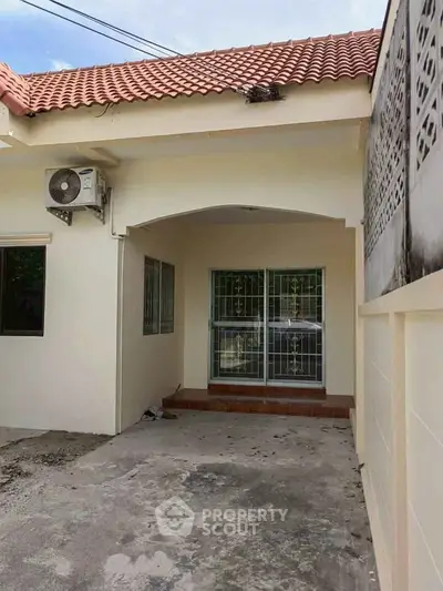 Charming single-story home with tiled roof and gated entrance, featuring an air conditioning unit for comfort.