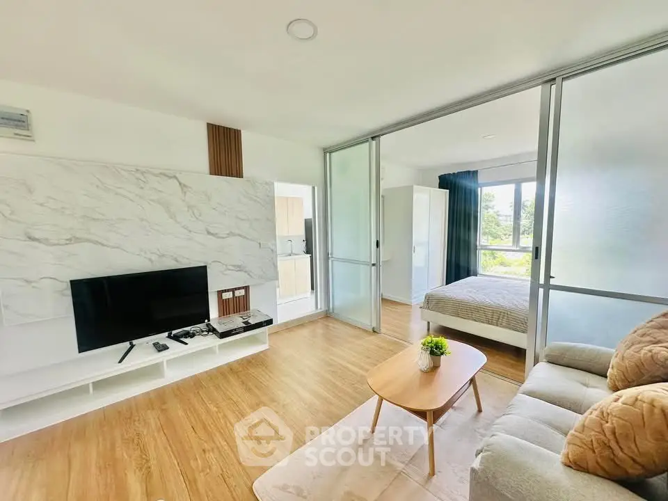 Modern open-plan living room with TV and cozy bedroom separated by sliding glass doors.