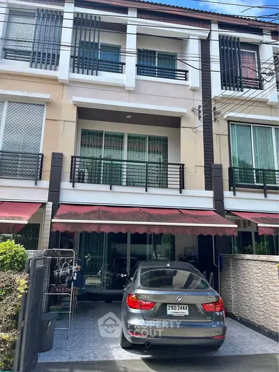 Modern three-story townhouse with car parked in driveway, featuring stylish facade and balcony.