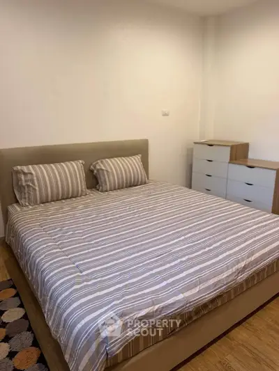 Cozy bedroom with striped bedding and modern dresser, perfect for relaxation.