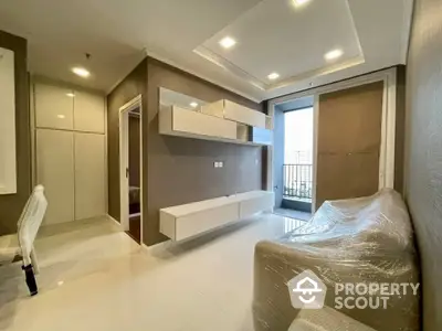 Spacious modern living room with sleek built-in cabinets and floating shelves, leading to a sunlit balcony with protective railing.