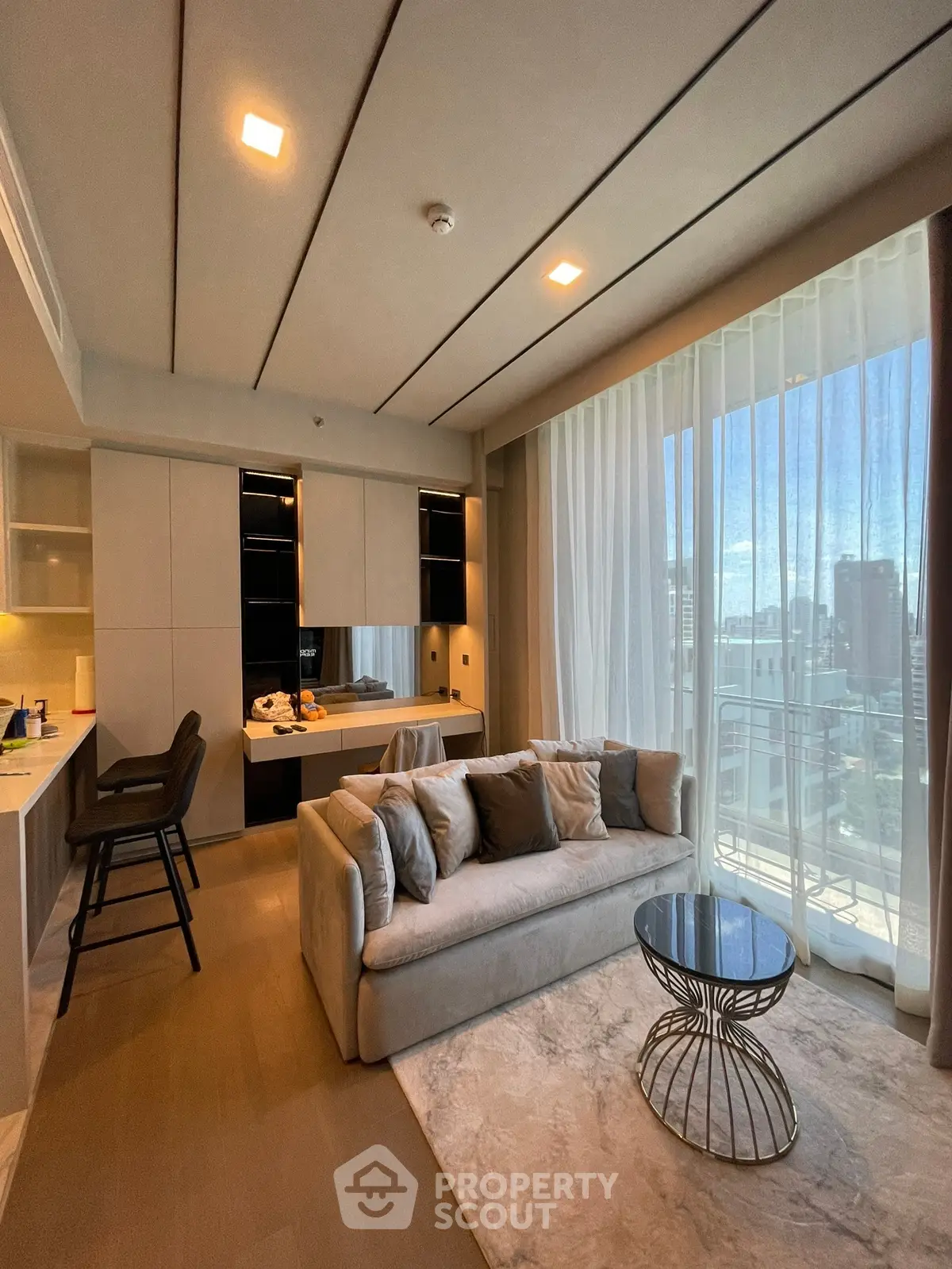 Modern living room with open kitchen and city view, featuring elegant furniture and natural light.