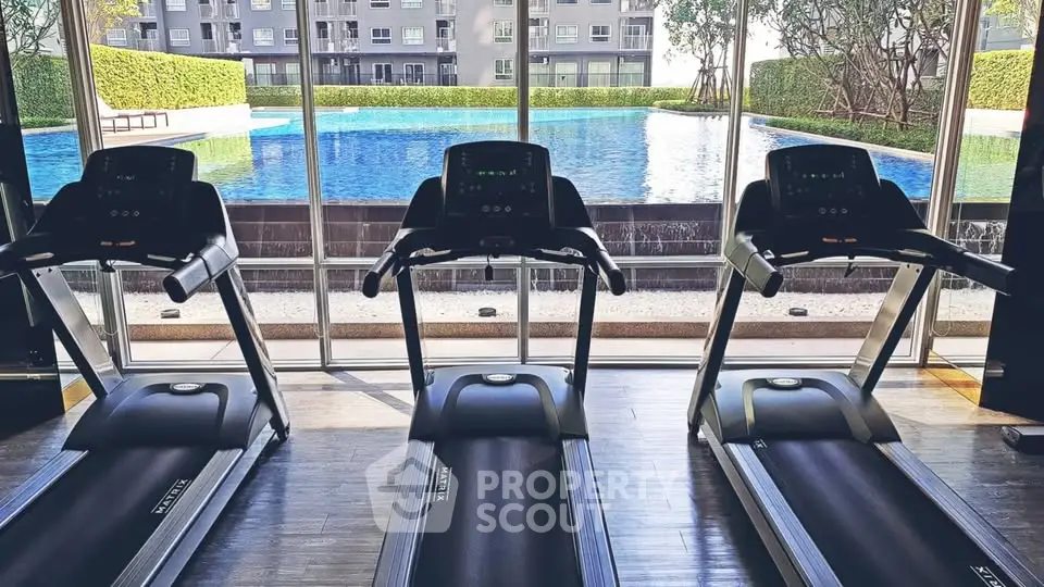 Modern gym with treadmills overlooking a luxurious pool and lush greenery.