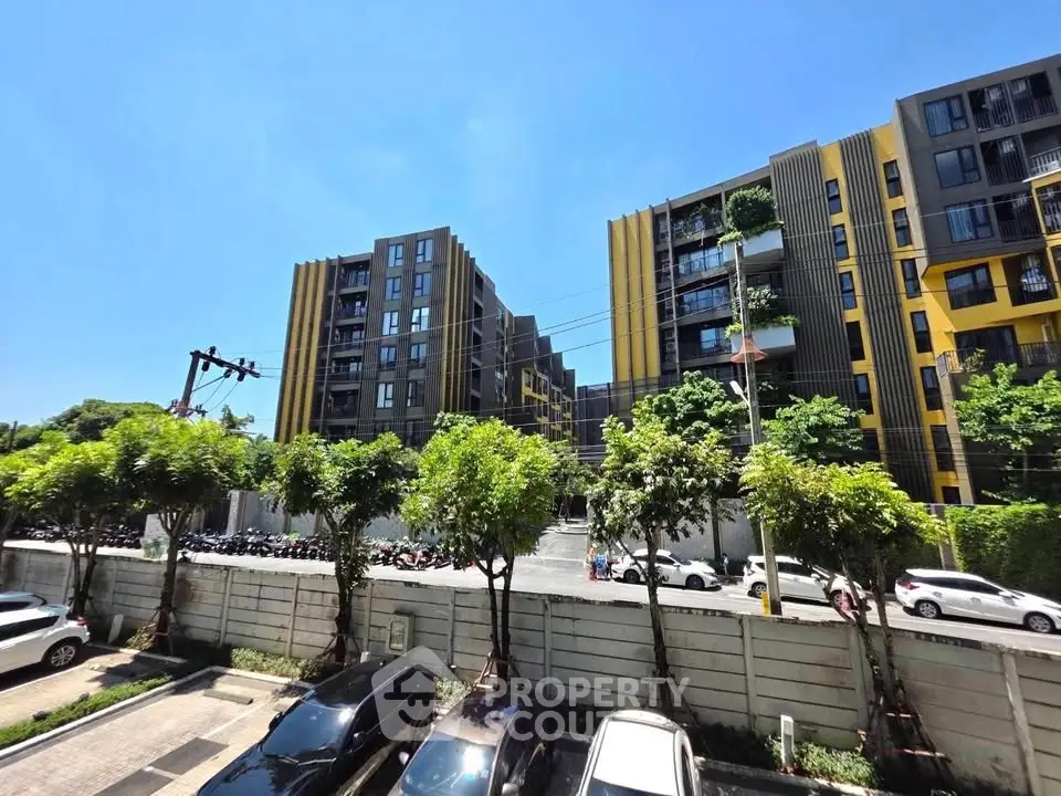 Modern apartment complex with vibrant yellow accents and lush greenery under a clear blue sky.
