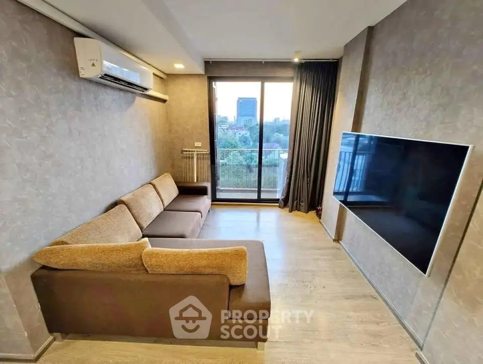 Modern living room with large sofa and wall-mounted TV, featuring a balcony with city view.