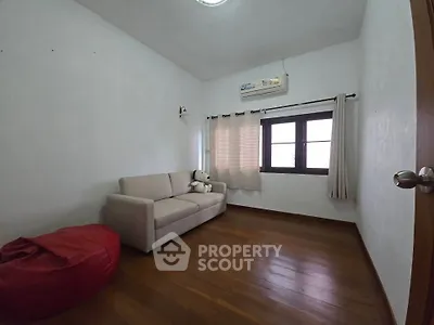 Cozy small living room with sofa and bean bag, wooden flooring, and window with curtains.