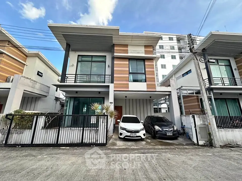 Modern townhouse with two cars parked in driveway, featuring sleek design and large windows.