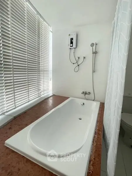 Modern bathroom with sleek bathtub and shower, featuring large window blinds for natural light.