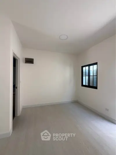 Spacious empty room with modern flooring and large window, perfect for customization.