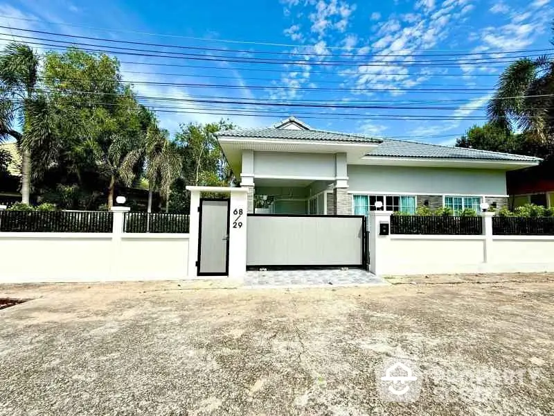 Charming single-story house with gated entrance and lush greenery under a clear blue sky.