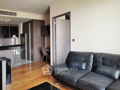 Modern living room with sleek black leather sofa and open kitchen layout in stylish apartment.
