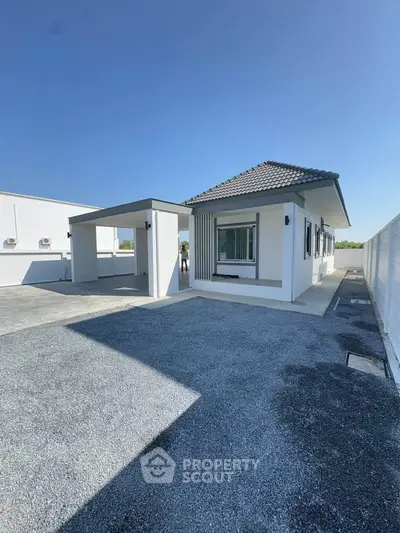 Modern single-story house with sleek design and spacious driveway under clear blue sky.