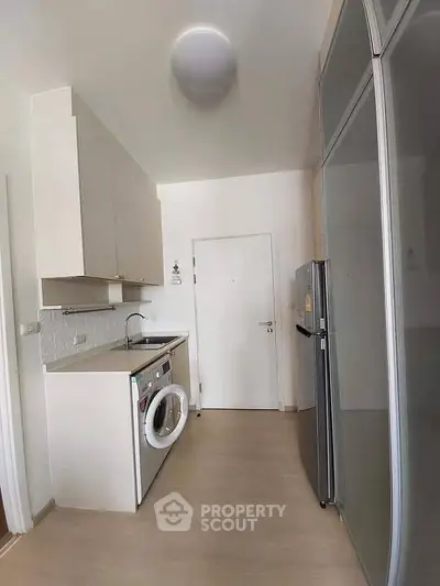 Modern kitchen with sleek appliances and compact design, featuring washing machine and fridge.