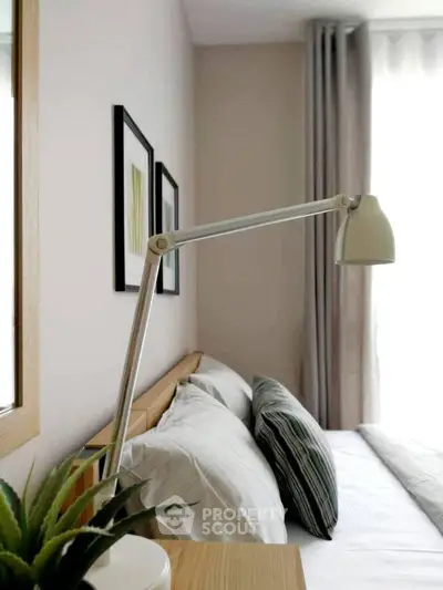 Cozy bedroom with modern decor and natural light, featuring stylish lamp and framed artwork.