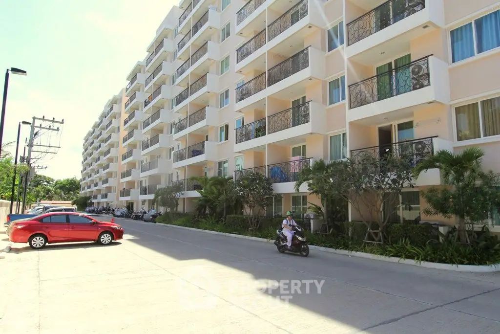 Modern apartment building with balconies and parking area in sunny setting.