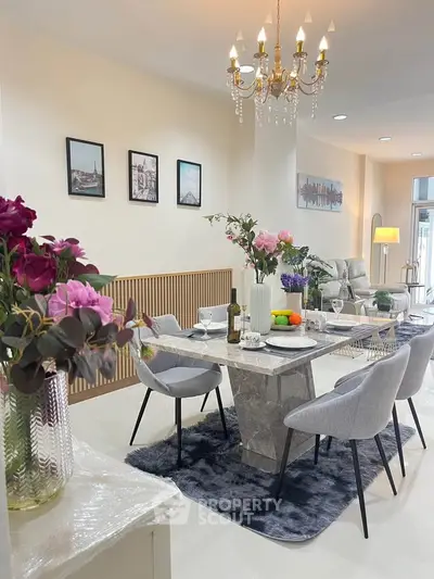 Elegant dining area with marble table, plush chairs, and chandelier in modern open-plan living space.