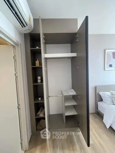 Modern bedroom with open wardrobe and air conditioning unit, showcasing sleek design and ample storage space.
