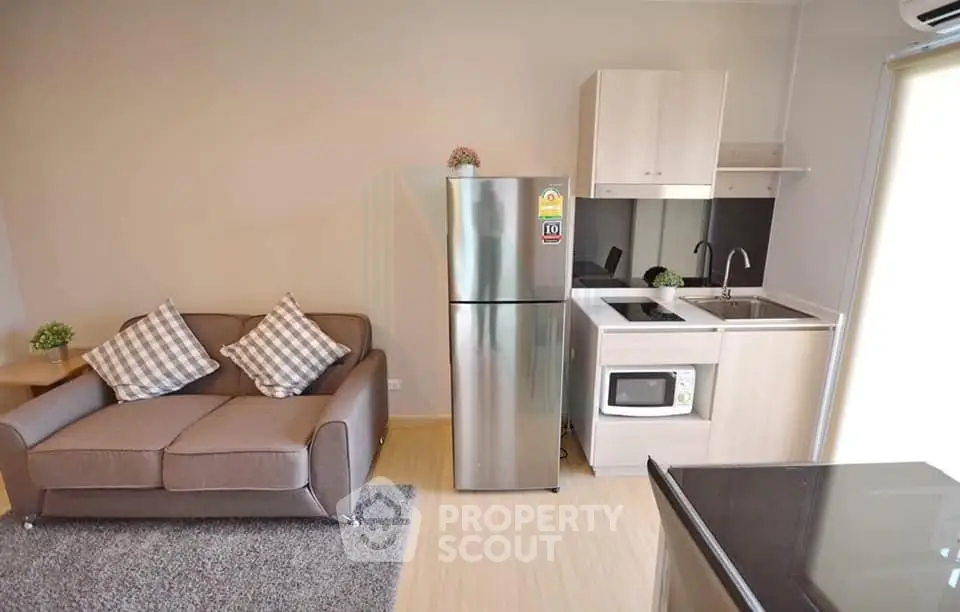 Modern compact living room with kitchenette featuring stainless steel fridge and cozy sofa.