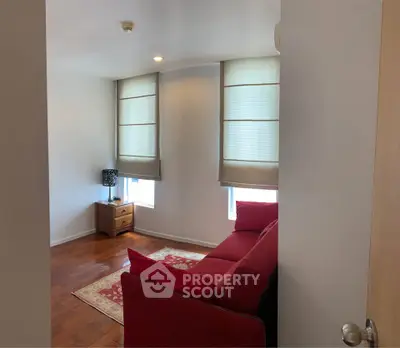 Cozy living room with red sofa and wooden flooring, featuring natural light from large windows.