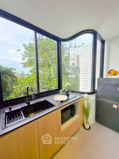 Modern kitchen with large windows and lush green view, featuring sleek appliances and minimalist design.