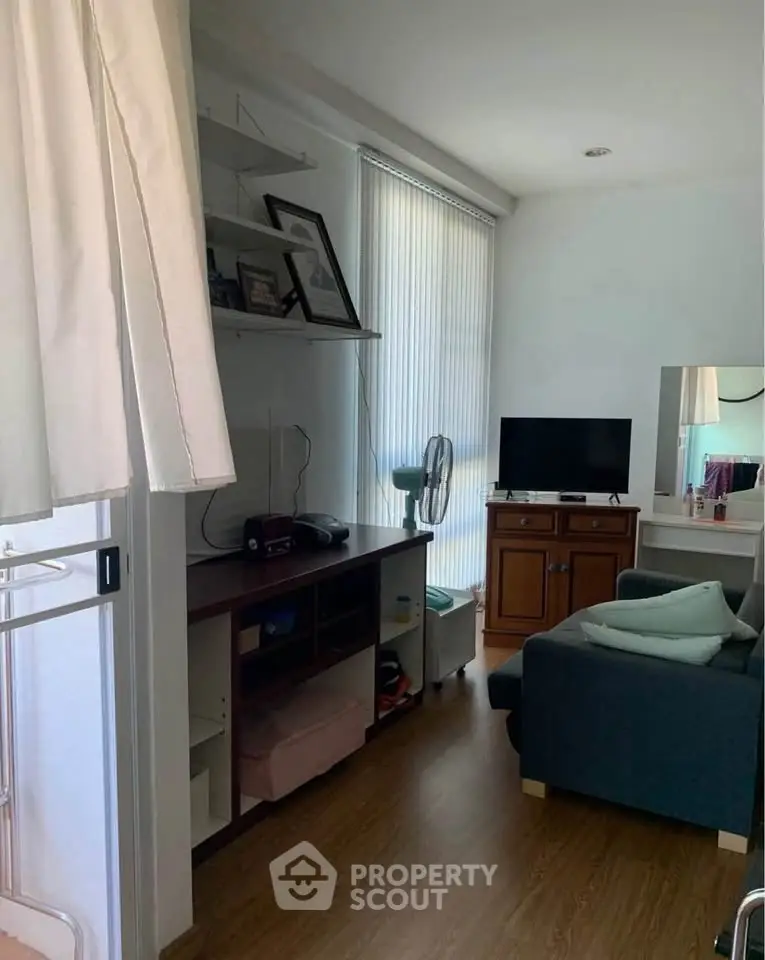 Cozy living room with natural light, featuring a TV, sofa, and shelving unit.