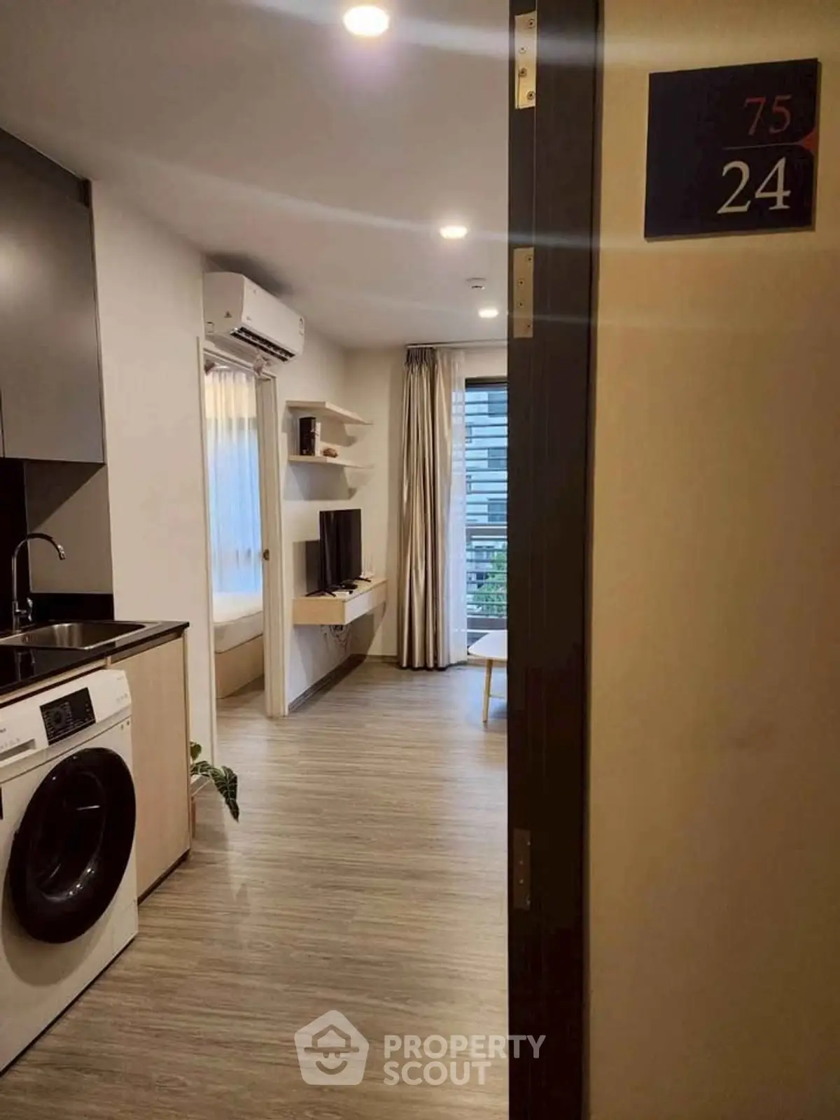 Modern apartment entrance with sleek kitchen and cozy living area, featuring built-in shelves and natural light.