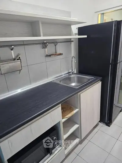 Modern kitchen with sleek cabinetry and stainless steel sink, featuring a black refrigerator and microwave.