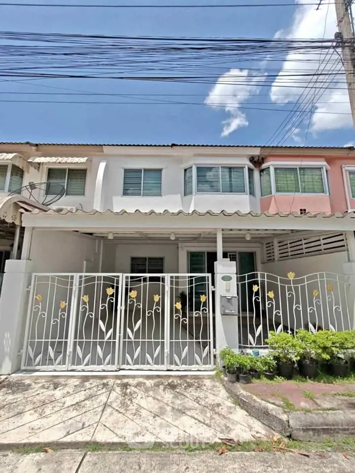 Charming townhouse with gated entrance and lush greenery under a clear blue sky.