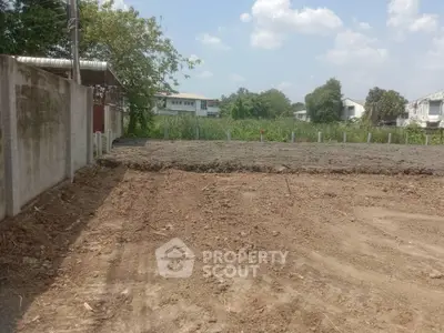 Spacious vacant lot ready for development, surrounded by a concrete wall and lush greenery, in a serene neighborhood.