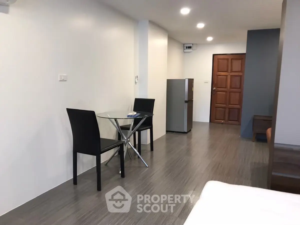 Modern apartment interior with dining area and fridge, featuring sleek design and ample lighting.