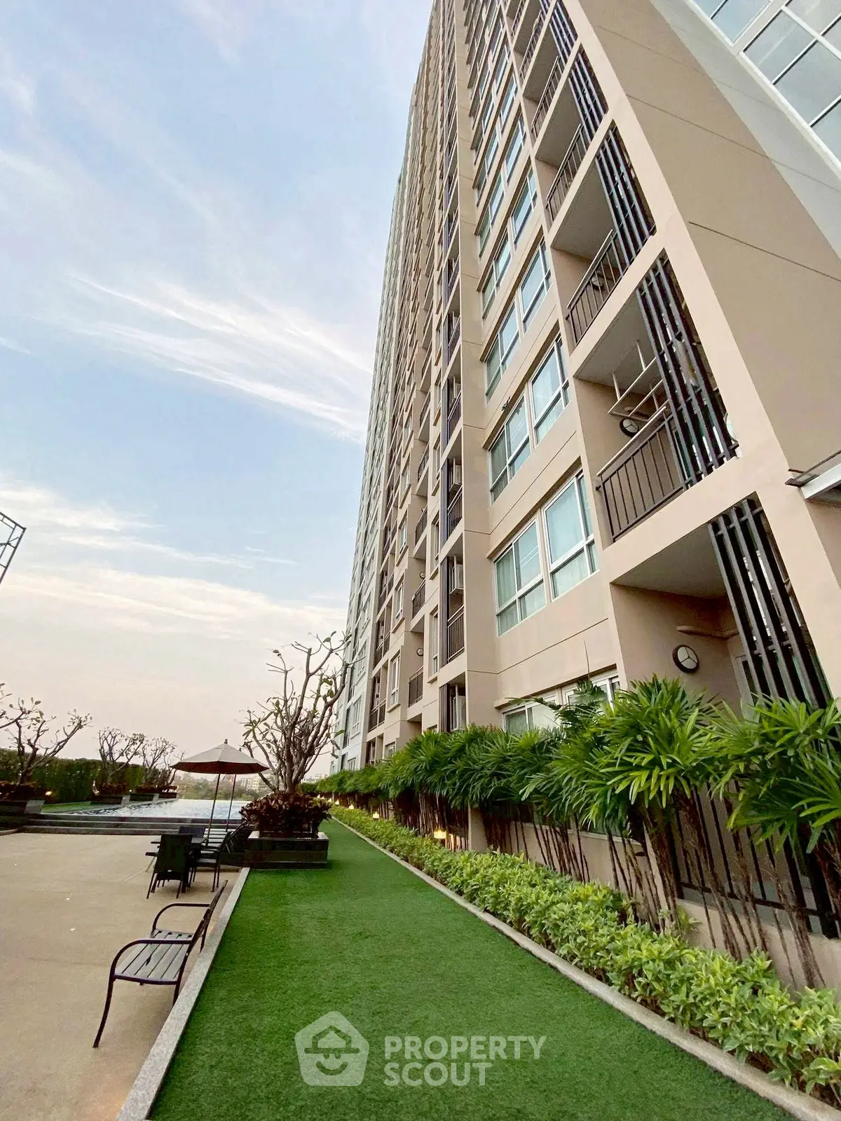 Modern high-rise building exterior with landscaped garden and seating area, perfect for urban living.