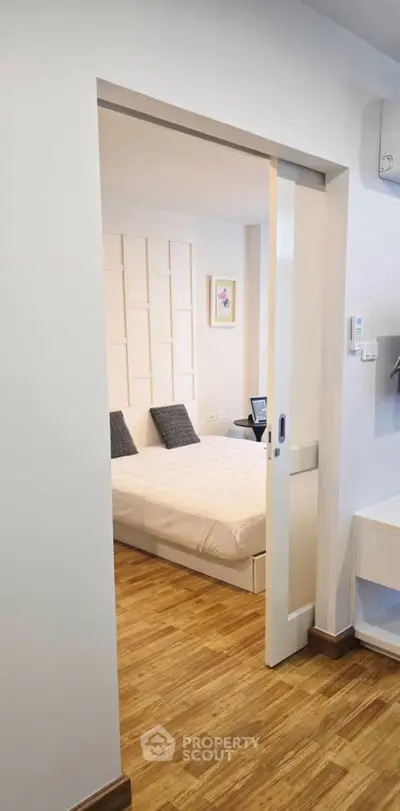 Modern bedroom with sliding door and wooden flooring, featuring a cozy bed and stylish decor.