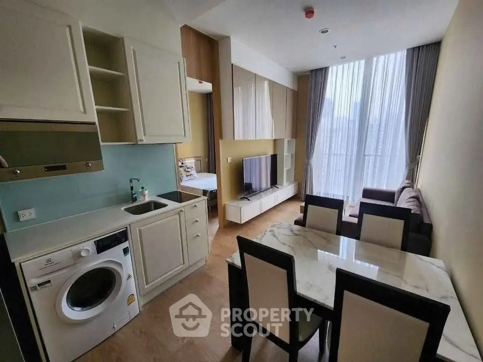 Modern living room with open kitchen and dining area, featuring a washing machine and stylish decor.