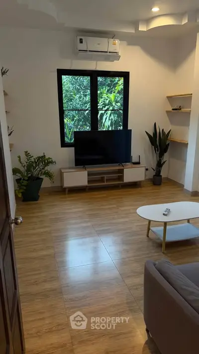 Modern living room with wooden flooring, stylish furniture, and large window with garden view.