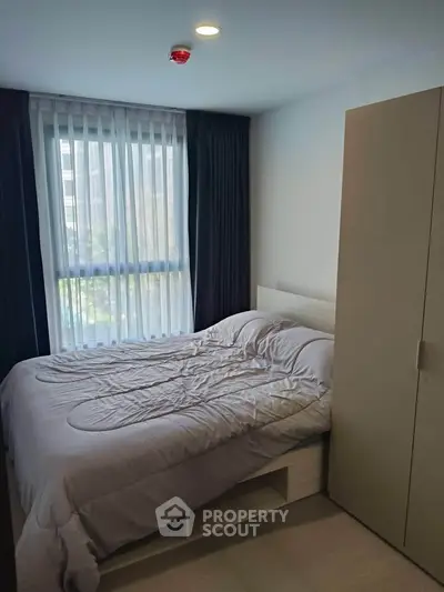 Cozy bedroom with modern furnishings and large window offering natural light.