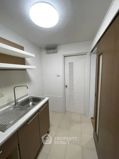 Compact kitchen with modern sink and shelving, featuring a sliding door and bright lighting.