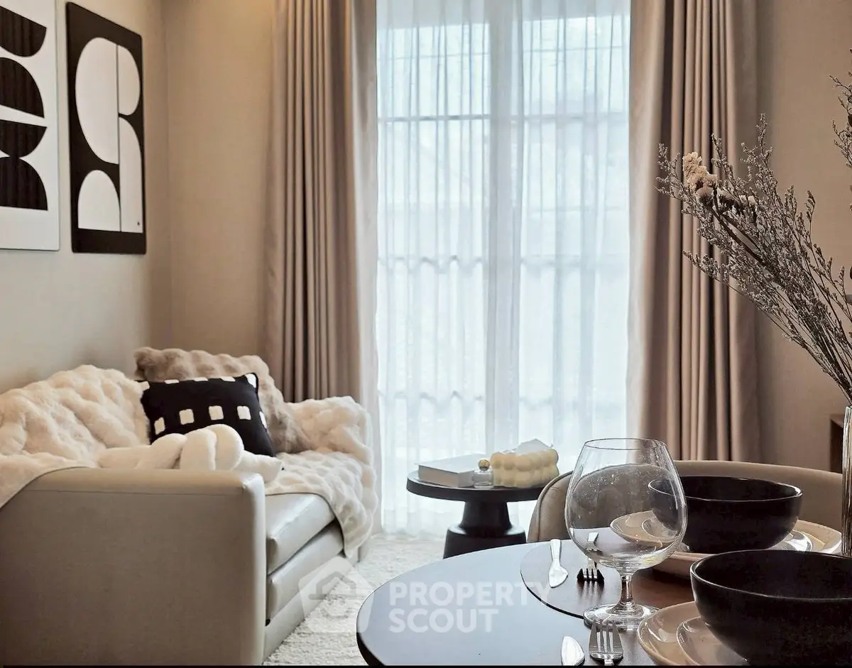 Elegant living room with modern decor and large window, featuring cozy seating and stylish artwork.