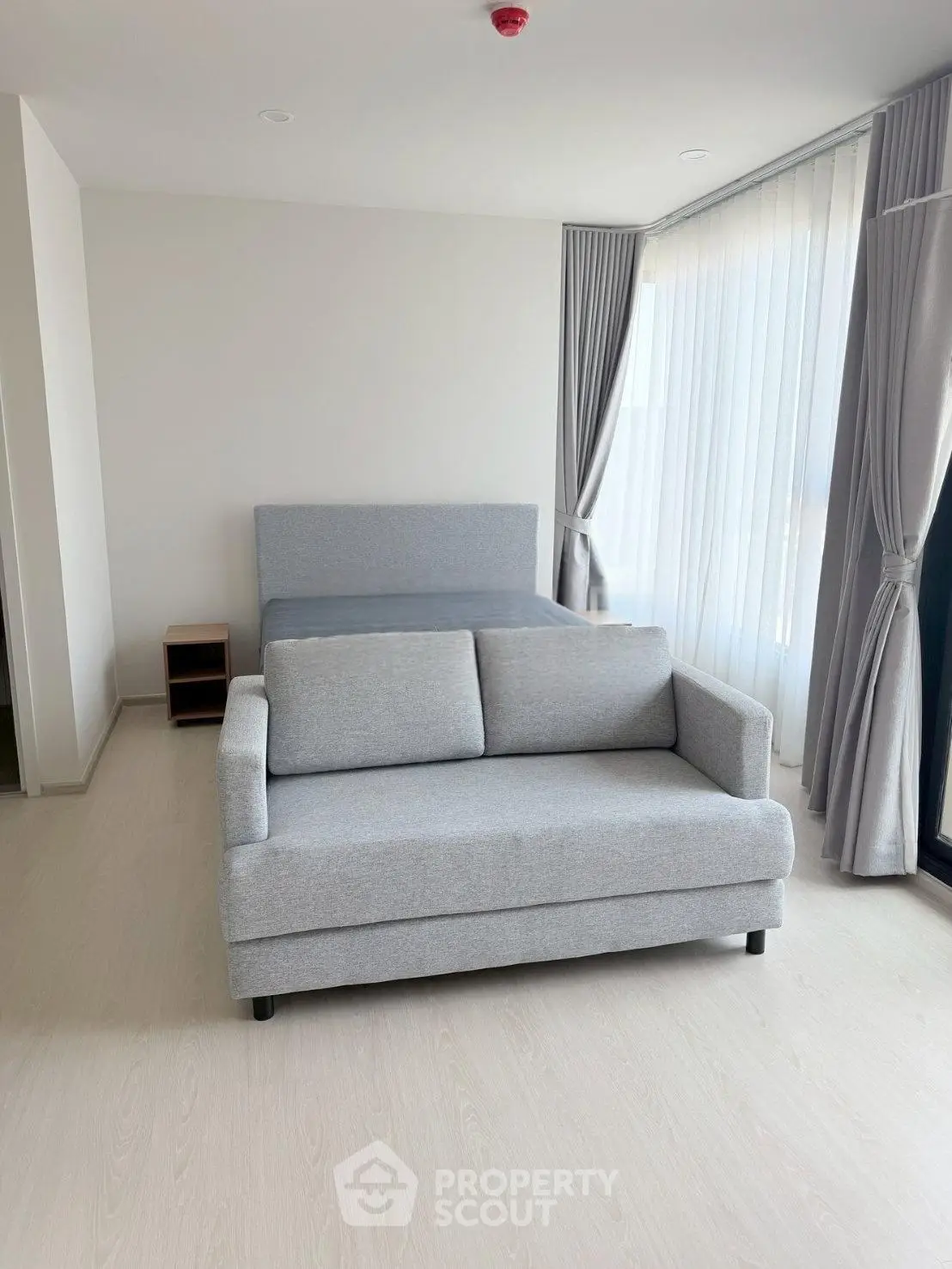 Modern studio apartment with stylish gray sofa and bed, featuring floor-to-ceiling windows and elegant curtains.