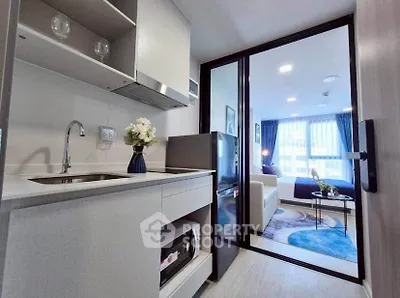 Modern compact kitchen with open layout leading to a cozy living area with large windows.