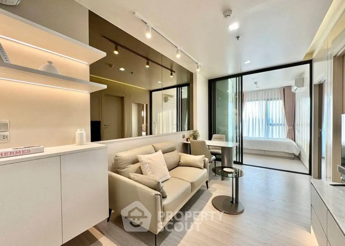 Modern open-plan living room with sleek furniture and glass partition to bedroom.