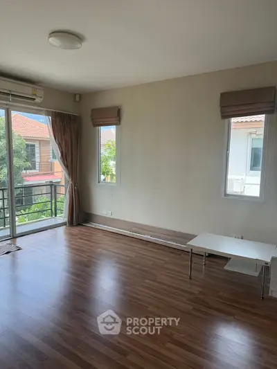 Spacious living room with wooden flooring and large windows offering natural light.