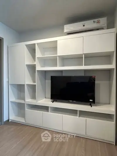 Modern living room with sleek white shelving and mounted TV, featuring minimalist design and air conditioning unit.