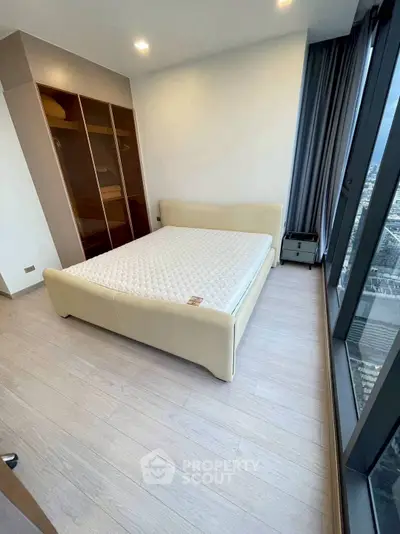 Modern bedroom with large windows and city view, featuring sleek wardrobe and minimalist design.