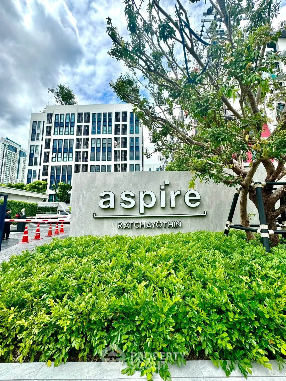 Modern condominium exterior with lush greenery at Aspire Ratchayothin, showcasing urban living.