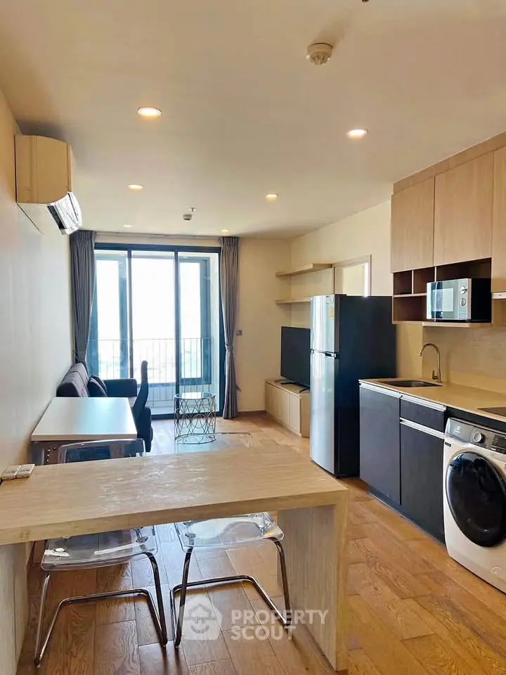 Modern open-plan living room with kitchen, featuring sleek appliances and a balcony view.